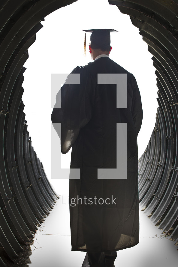 man walking through a tunnel in his cap and gown on graduation day