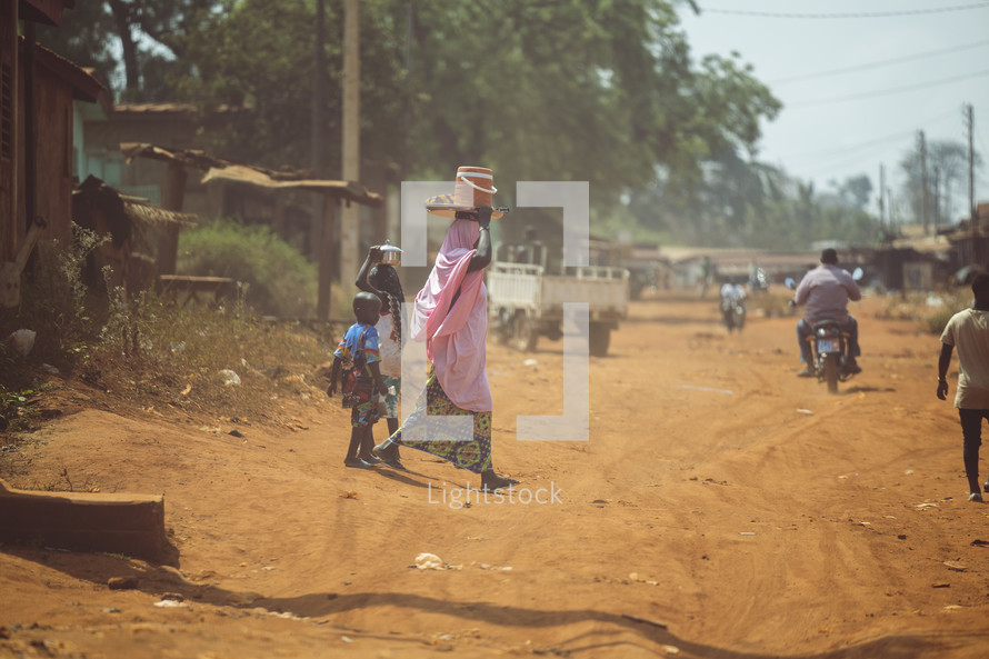 African mother walking with her children, carrying stuff on her head in a small village of the Ivory Coast in West Africa