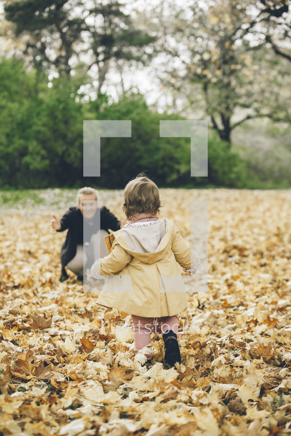toddler running through fall leaves to get to mom 