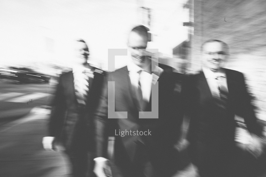 A couple of groomsmen walking down a street in a blur. 