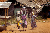 African children walking with pots on their head in the Dusty small village of The Ivory Coast in west Africa