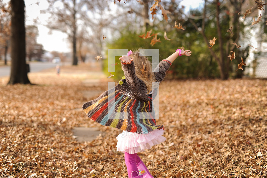 a toddler girl tossing fall leaves into the air 