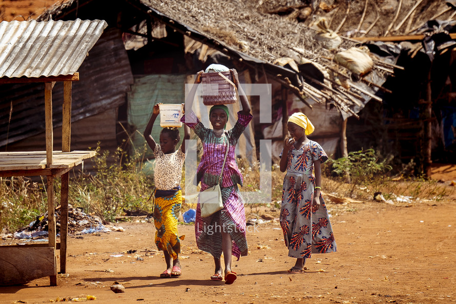 African children walking with pots on their head in the Dusty small village of The Ivory Coast in west Africa