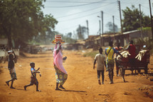 African mother walking with her children, carrying stuff on her head in a small village of the Ivory Coast in West Africa