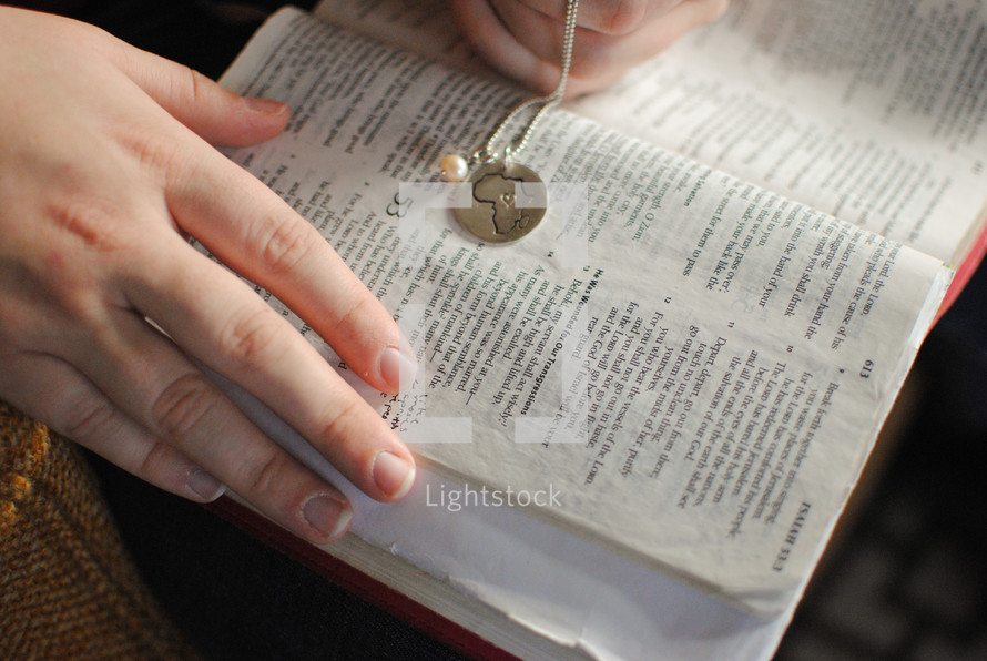 a woman holding a charm of Africa over the pages of a Bible 