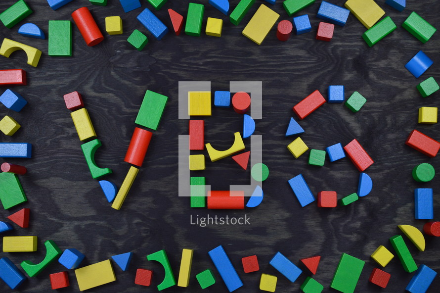 the letters VBS out of colorful wooden toy blocks on black background 