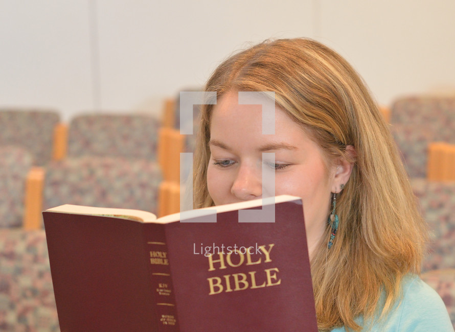 Young blond woman smiling while reading in the bible sitting in church. 
