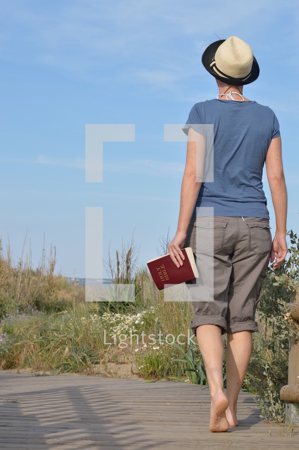 woman walking with bible in hand in the dunes near the beach