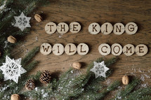 star ornaments, pine cones, snow, pine boughs and the words THE KING WILL COME on wooden slices