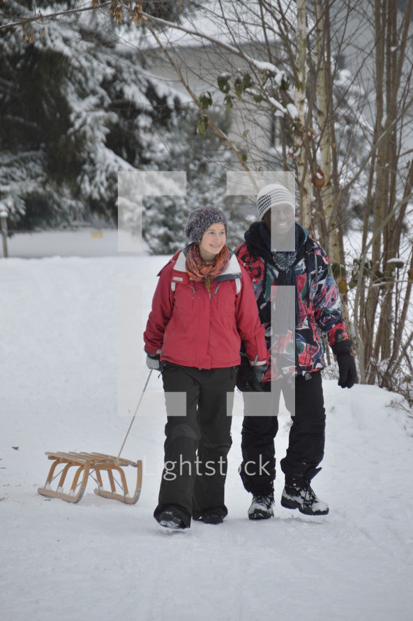young couple walking hand in hand in the snow and pulling their sled behind