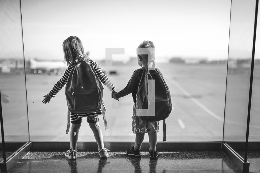 siblings looking out a window at an airport 