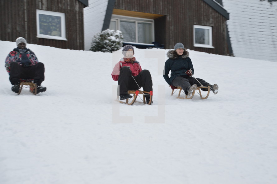 adults sledding down a snowy slope 