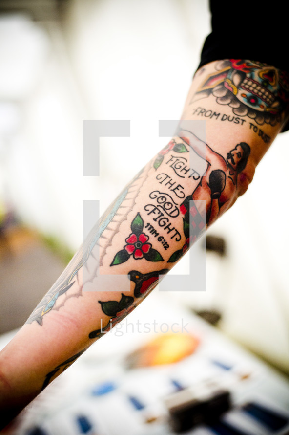 Arm with a "fight the good fight" tattoo.