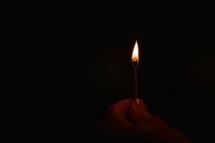 Hand holding burning matchstick in the darkness. 