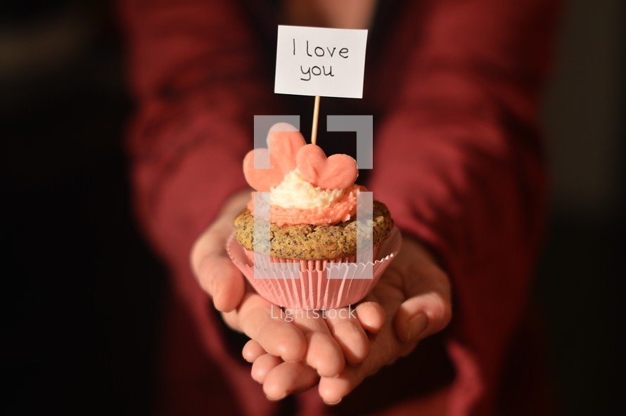 Woman offering a cupcake with pink hearts and a sign saying I LOVE YOU. 
