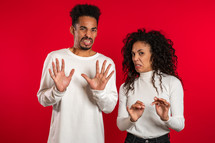 Young african couple standing on red studio background expressing discontent and showing disgust, aversion gesture at camera. Portrait of man and woman with sign of dislike, stop.