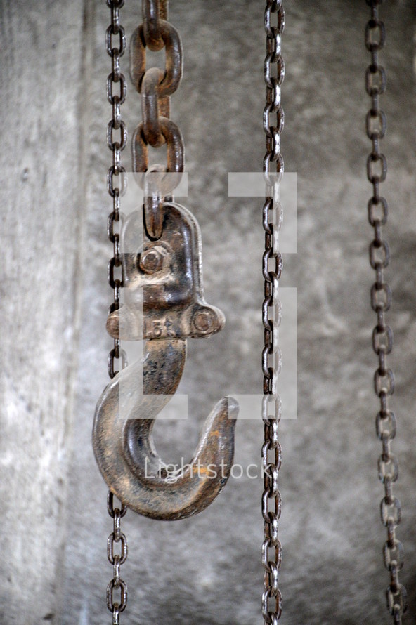A large hook and chains. 
hook, chains, chain, industrial, hoist, hang, building, hang up, caught, snag, lock, raise, raising, pull, pulling, up, down, hike up, hoisting, lift, lifting, wind, winding, bound, trussed, tied, metal, ferric, iron 