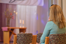 a young blond woman sitting alone in prayer in a modern church 
