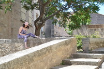 a woman reading a book sitting on a stone wall 