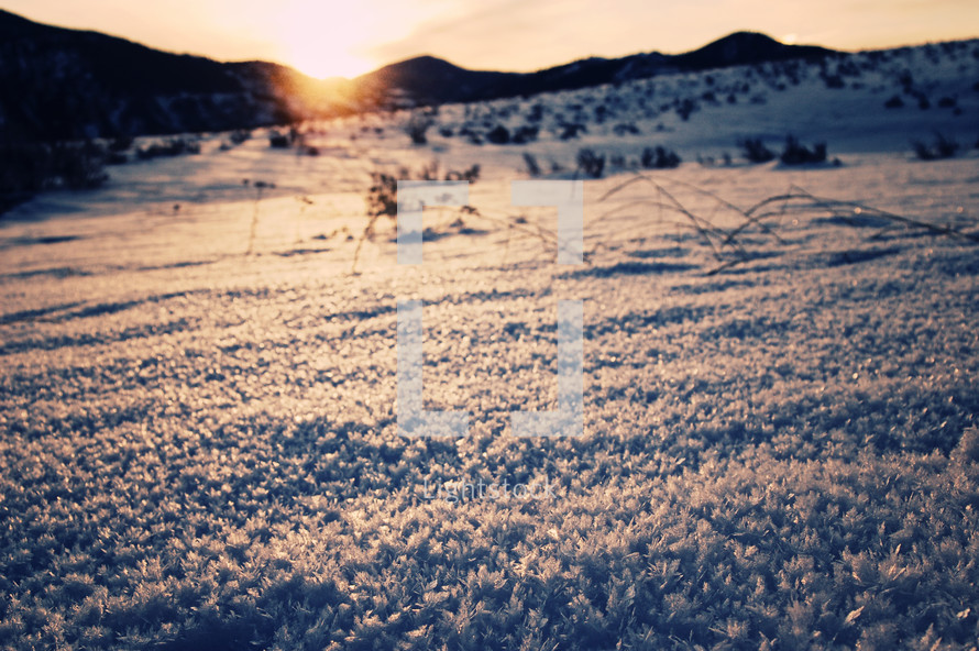 Snow-covered terrain and the silhouette of mountains at sunrise. 