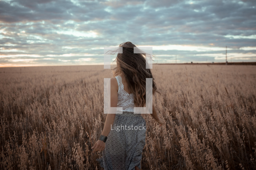 a woman walking through a field of brown grasses 