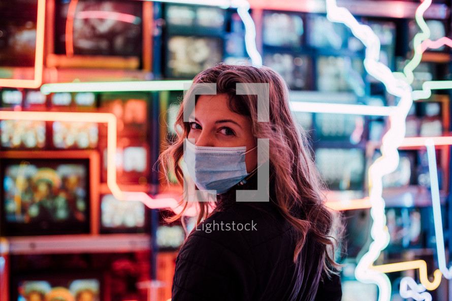 young woman wearing a face mask standing in front of a storefront window 