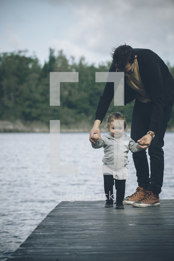 father and toddler child walking on a dock 