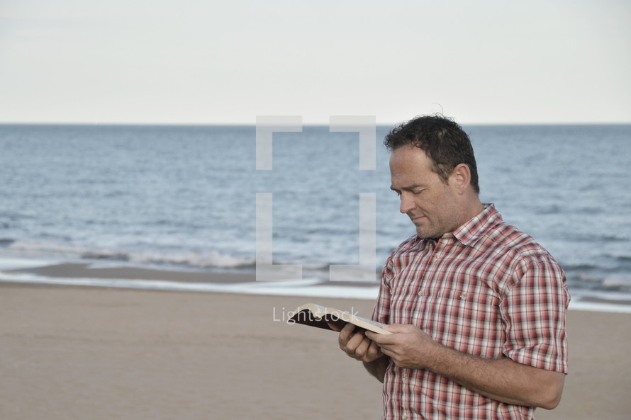 a man reading a Bible on a beach 