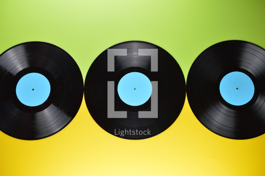 three old black vinyl records with blank cyan labels on yellow and green background