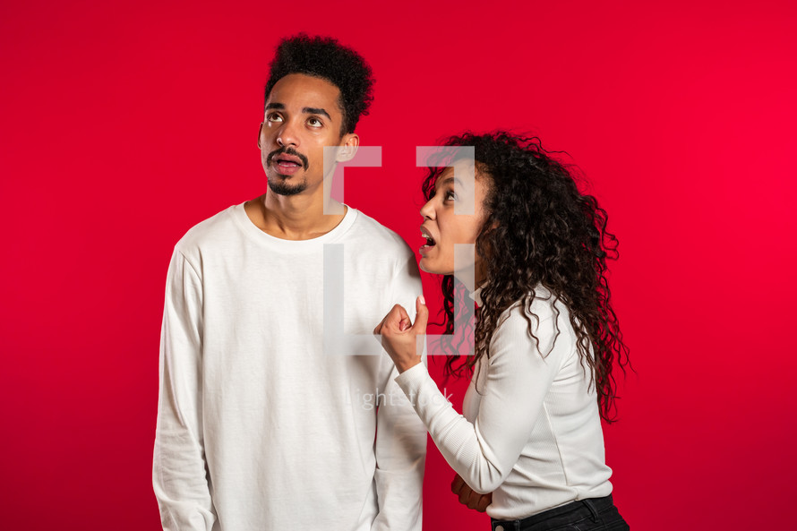 african woman emotionally screaming at her husband or boyfriend on red background in studio. Bored man rolling his eyes. Concept of conflict, problems in relationships