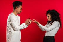 Young couple. African man makes marriage proposal to his lover woman with ring on red studio background but disappointed upset girl doesn't like gift