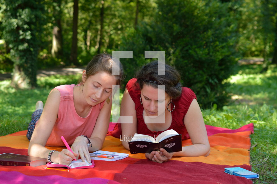 women reading Bibles on a blanket in the grass 