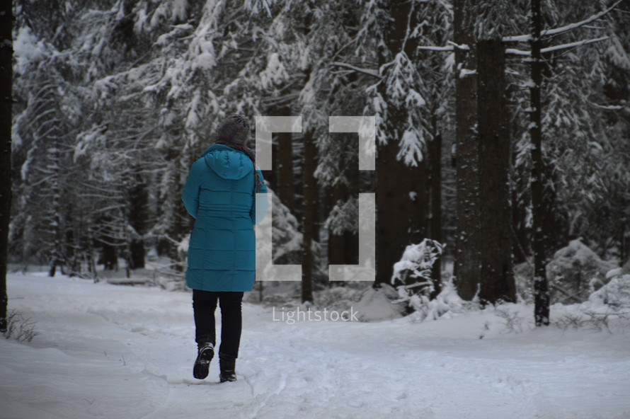 a woman in a coat walking through the snow in a winter forest 