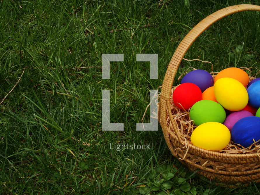 Basket of colored Easter eggs in the grass.
