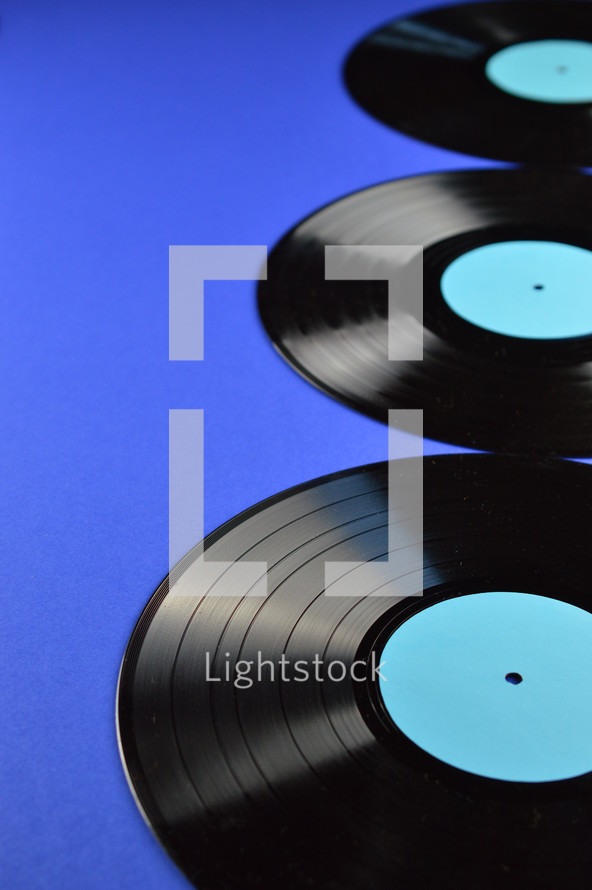 three old black vinyl records with blank cyan labels on blue background