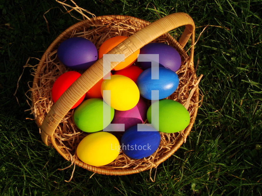 Multicolored Easter eggs in a basket, in the grass.

