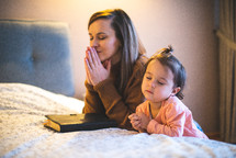 a mother and daughter praying bedside 