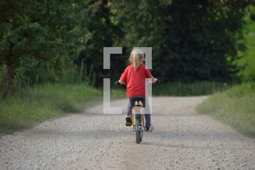 a little girl riding a bicycle on a gravel road 