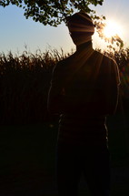 a young man standing beside a corn field 