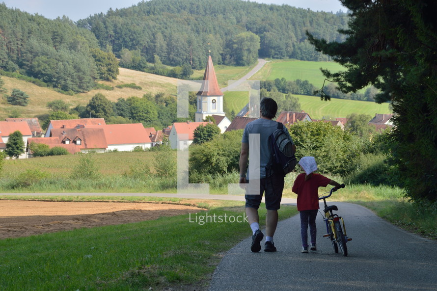 father and daughter walking down a rural road into town 