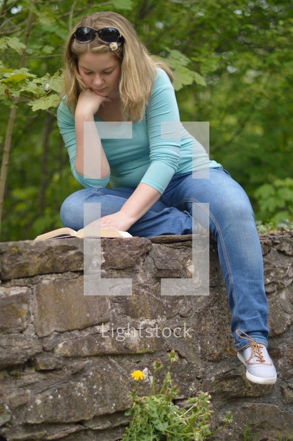 a woman sitting on a stone wall reading a Bible 
