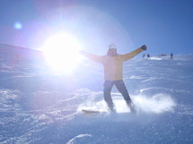 A man snowboarding down a mountain with the sun glaring behind him.