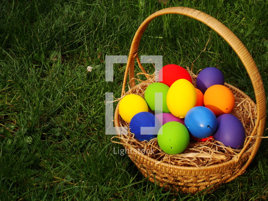 Multicolored  Easter eggs in a basket in the grass. 
