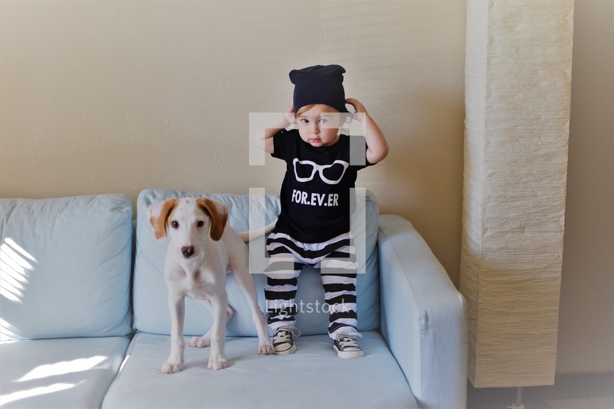 a toddler boy and dog standing on a couch 