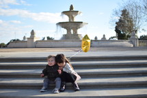 children sitting on steps in front of a fountain