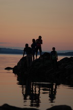 Silhouette of a family on a rock in the ocean at sunset.