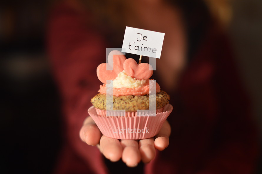 Woman offering a cupcake with pink hearts and a sign saying JE T'AIME, which means: I LOVE YOU. 