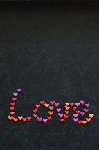 the word LOVE written with many little colorful clay hearts on black background