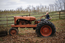 a boy child sitting on a tractor on a farm 