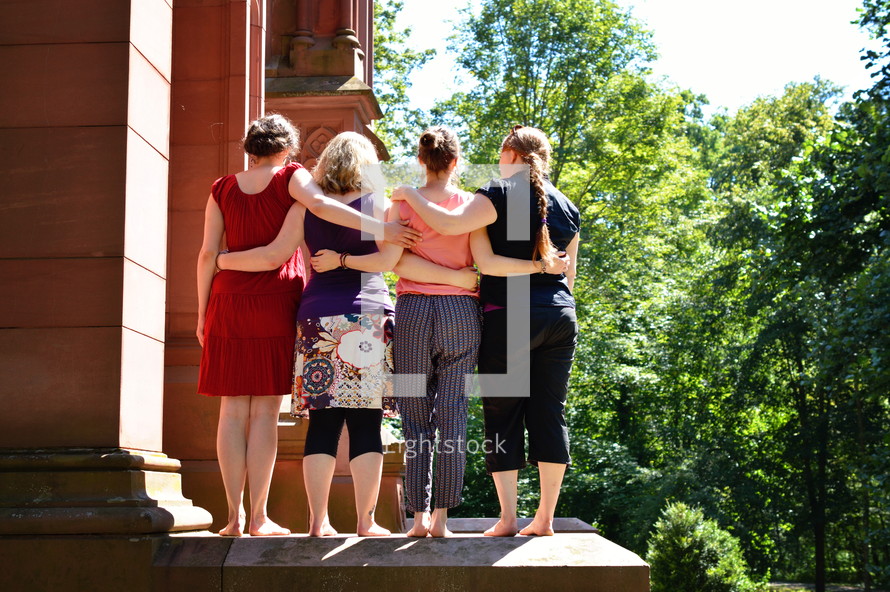 women standing in front of a church with arounds around each other 